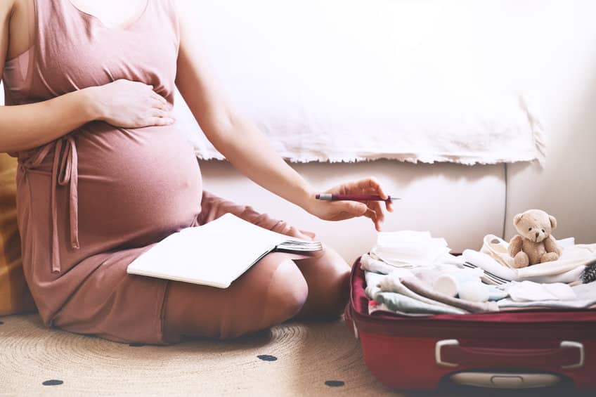 pregnant woman packing bag for maternity hospital, making notes,